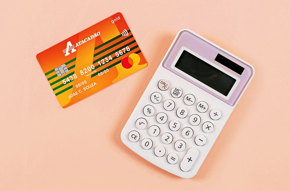 Fundo cor de rosa. Uma calculadora ao lado de um Cartão Atacadão.